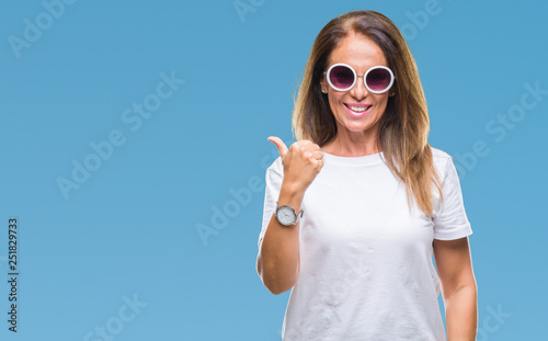 Middle age hispanic woman wearing fashion sunglasses over isolated background doing happy thumbs up gesture with hand. Approving expression looking at the camera with showing success.