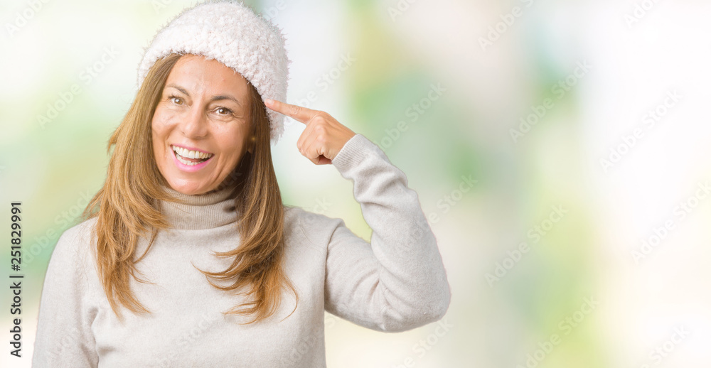 Beautiful middle age woman wearing winter sweater and hat over isolated background Smiling pointing to head with one finger, great idea or thought, good memory Beautiful middle age woman wearing winter sweater and hat over isolated background Smiling pointing to head with one finger, great idea or thought, good memory