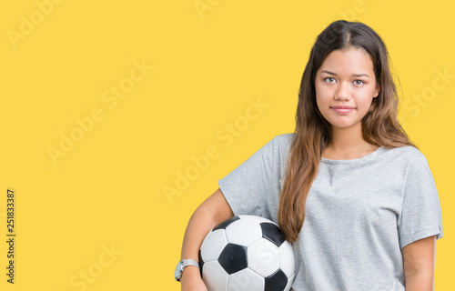 Young beautiful brunette woman holding soccer football ball over isolated background with a confident expression on smart face thinking serious © Krakenimages.com