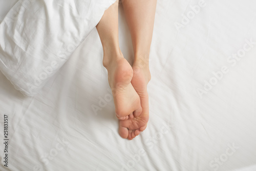 Woman legs in white bed sheets. Skincare concept
