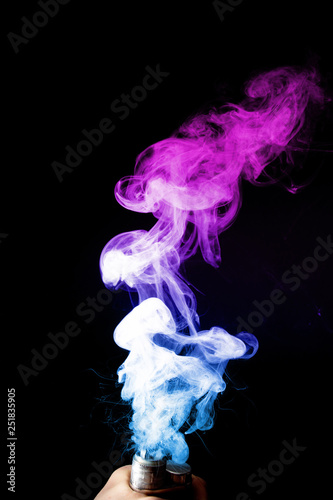 Male hand holds vape upside down. Vape clouds splash from coil on black background. Fog is white. Stock isolated white smoke with spray boiling glycerine.