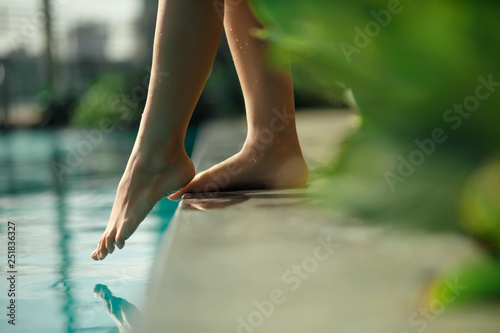 Closeup young female leg touch blue water in swimming pool