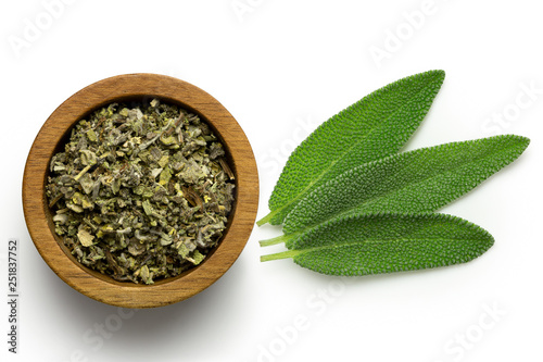 Photography Dried rubbed sage in a dark wood bowl next to fresh sage leaves isolated on white from above