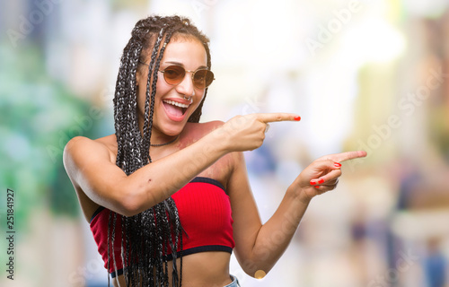 Young braided hair african american with birth mark wearing sunglasses over isolated background smiling and looking at the camera pointing with two hands and fingers to the side.