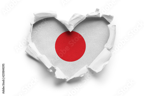 Heart shaped hole torn through paper, showing satin texture of flag of Japan. Isolated on white background