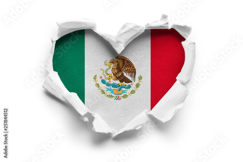 Heart shaped hole torn through paper, showing satin texture of flag of Mexico. Isolated on white background photo