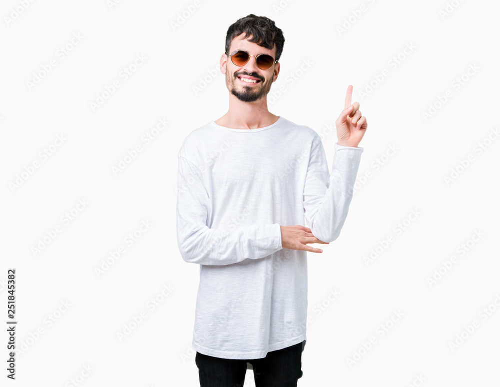 Young handsome man wearing sunglasses over isolated background with a big smile on face, pointing with hand and finger to the side looking at the camera. Young handsome man wearing sunglasses over isolated background with a big smile on face, pointing with hand and finger to the side looking at the camera.