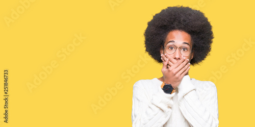 Young african american man with afro hair wearing glasses shocked covering mouth with hands for mistake. Secret concept.