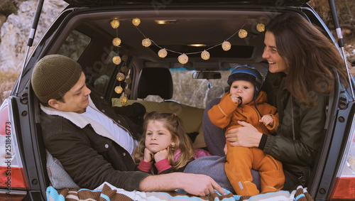 Happy Family  sitting in the open trunk of a black car with kids  against the backdrop of autumn mountains