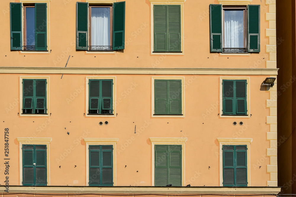 Close-up of a yellow building façade with rows of windows and green shutters, Genoa, Liguria, Italy