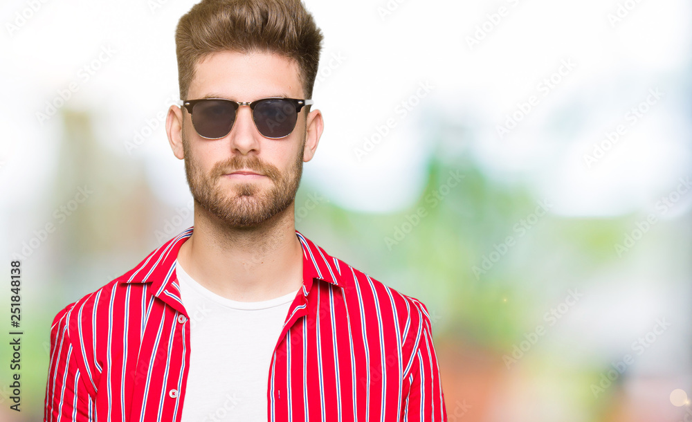 Young handsome man wearing sunglasses with serious expression on face. Simple and natural looking at the camera. Young handsome man wearing sunglasses with serious expression on face. Simple and natural looking at the camera.