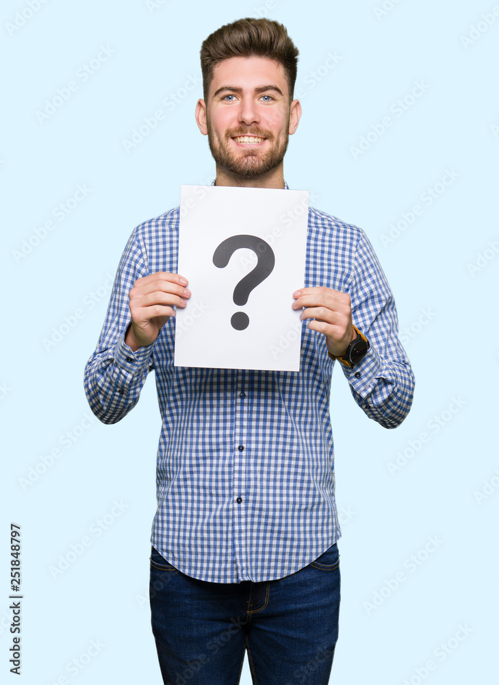 Young handsome man holding paper with question mark with a happy face standing and smiling with a confident smile showing teeth Young handsome man holding paper with question mark with a happy face standing and smiling with a confident smile showing teeth