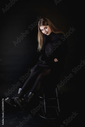 portrait of a young girl in a black dress on a dark background sitting in the studio