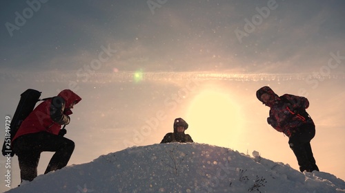 team work and victory. Tourists come to top of snowy hill and rejoice at victory against backdrop of yellow sunset. teamwork of people in difficult conditions.
