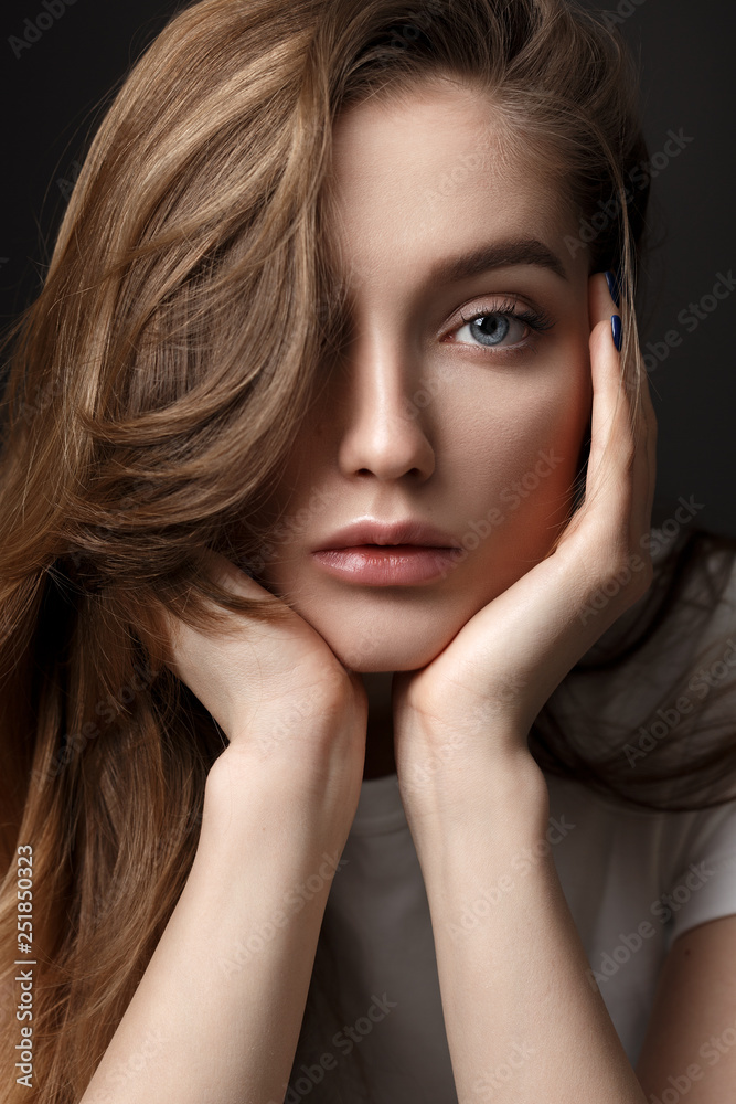 Obraz premium Portrait of beautiful brunette girl with long flowing hair dressed in white t-shirt on the dark background in the studio