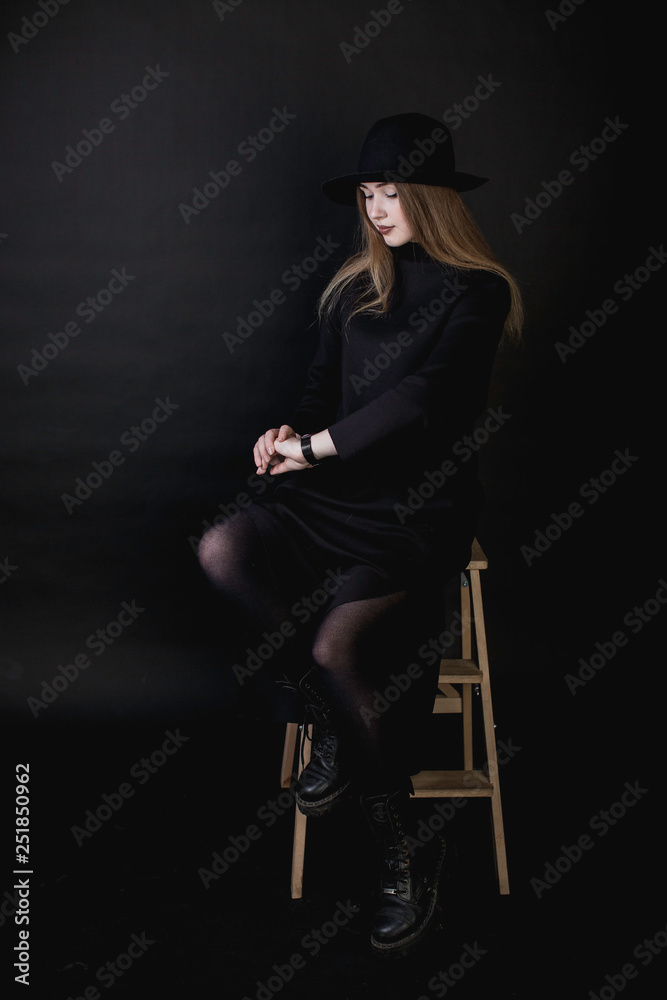 portrait of a young girl in a black dress and a hat on a dark background in the studio