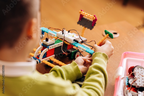 Vászonkép Sedulous boy dressed in green sweater sits at the table in the robotics school a