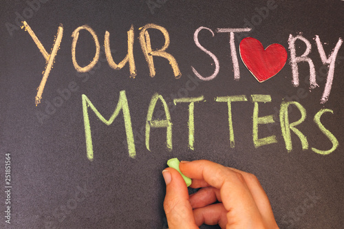 your story matters phrase handwritten on blackboard with heart symbol instead of O, hand holding green chalk