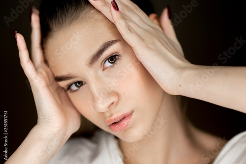 Portrait of young beautiful brown-eyes girl with natural makeup holding her hands on her head