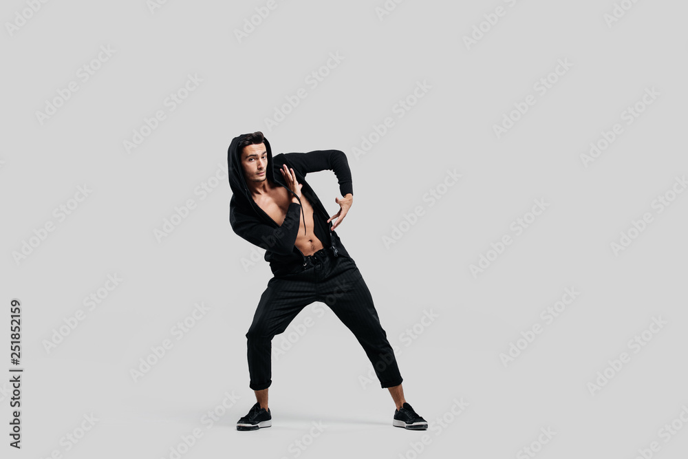 Young handsome young dancer dressed in black pants, a sweatshirt on a naked torso is dancing street dance. He makes stylized movements with his hands