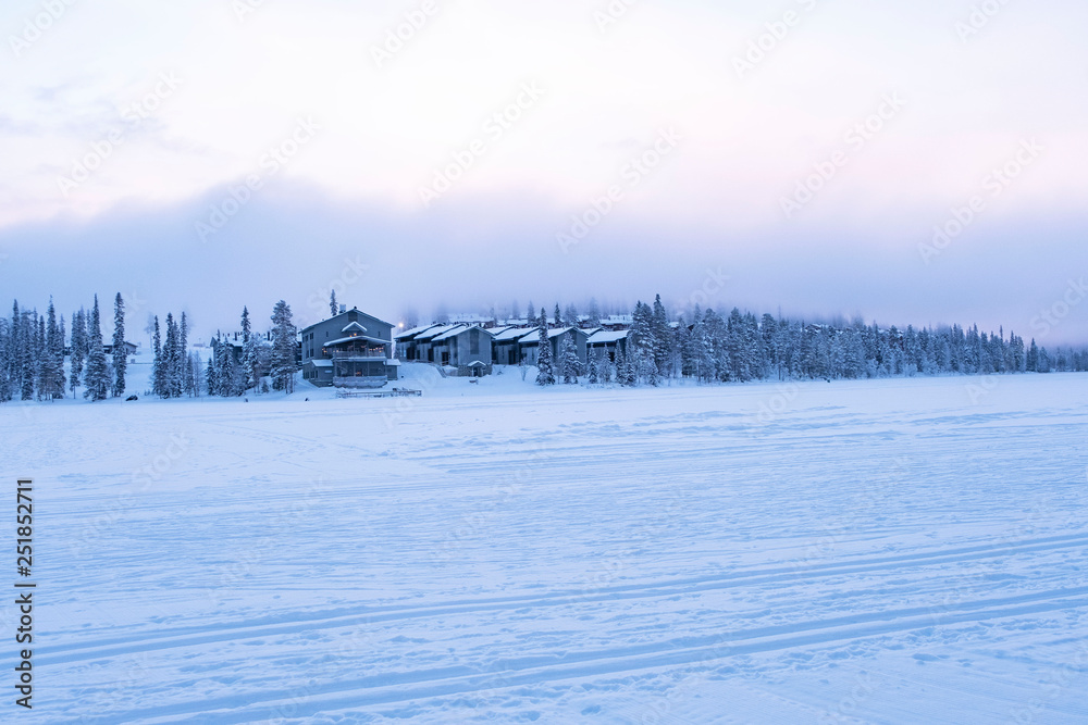 Winter landscape. Tourist complex, wooden houses on the lake among the trees. Winter lake in Finland Lapland, Ruka mountain. Winter landscape. Tourist complex, wooden houses on the lake among the trees. Winter lake in Finland Lapland, Ruka mountain.