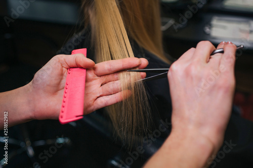 Close-up of hairdressers hand cutting blonde hair. Doing new haircut in beauty salon