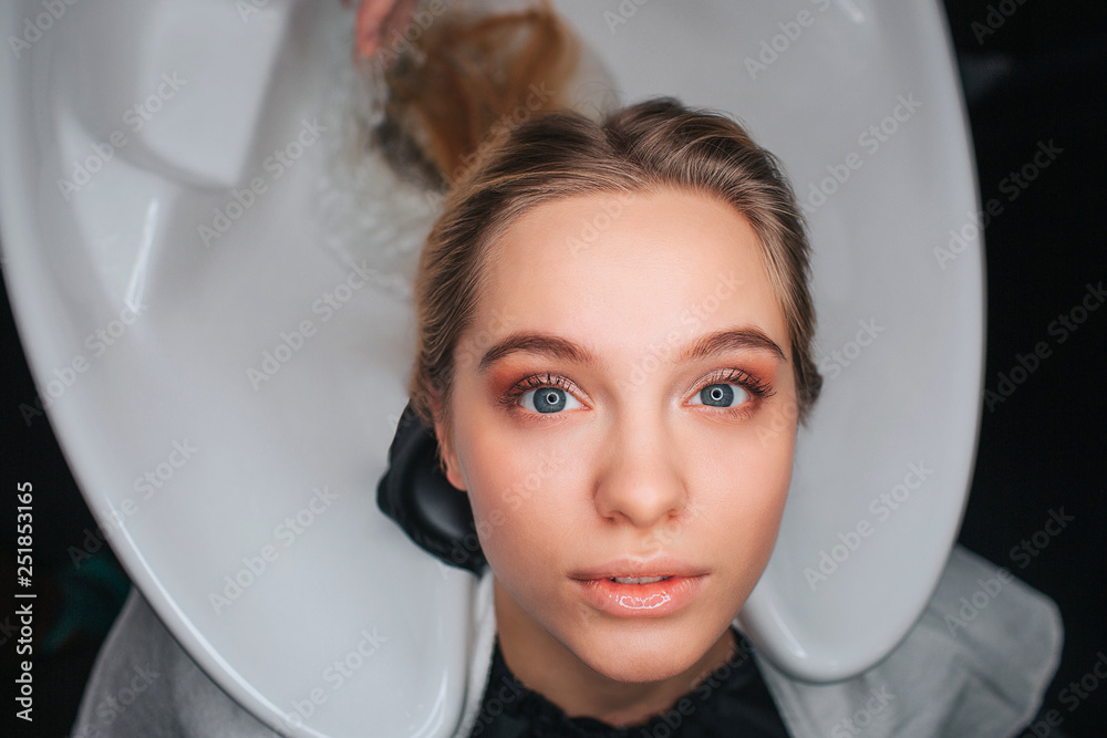 Portrait of blonde beautiful young woman sitting on white hair wash sink and waiting for a hairdresser. Washing hair in beauty salon Portrait of blonde beautiful young woman sitting on white hair wash sink and waiting for a hairdresser. Washing hair in beauty salon