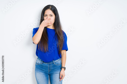 Beautiful brunette woman over isolated background smelling something stinky and disgusting, intolerable smell, holding breath with fingers on nose. Bad smells concept.
