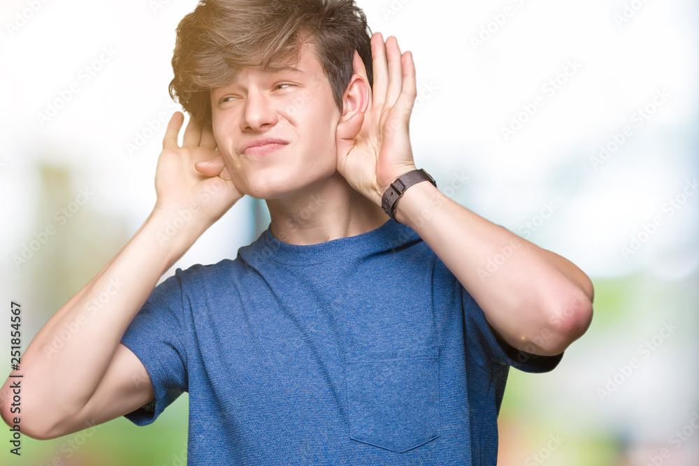Young handsome man wearing blue t-shirt over isolated background Trying to hear both hands on ear gesture, curious for gossip. Hearing problem, deaf
