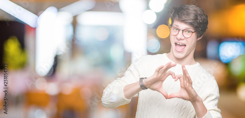Young handsome man wearing glasses over isolated background smiling in love showing heart symbol and shape with hands. Romantic concept.