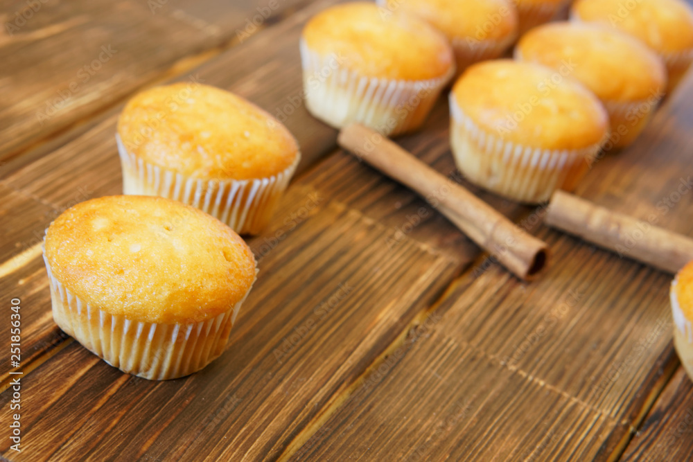 Bright golden cupcakes and cinnamon sticks lie on a wooden surface made of pine boards. Tasty and healthy food. Daylight Bright golden cupcakes and cinnamon sticks lie on a wooden surface made of pine boards. Tasty and healthy food. Daylight