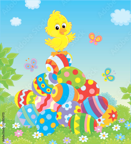 Little yellow Easter Chick on a pile of colorfully decorated eggs on green grass on a sunny spring day, vector illustration in a cartoon style