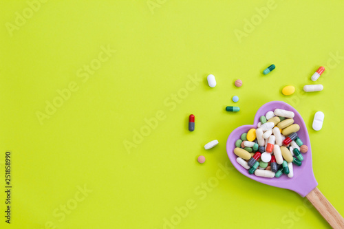 Assorted pharmaceutical medicine pills, tablets and capsules on wooden hearted spoon 