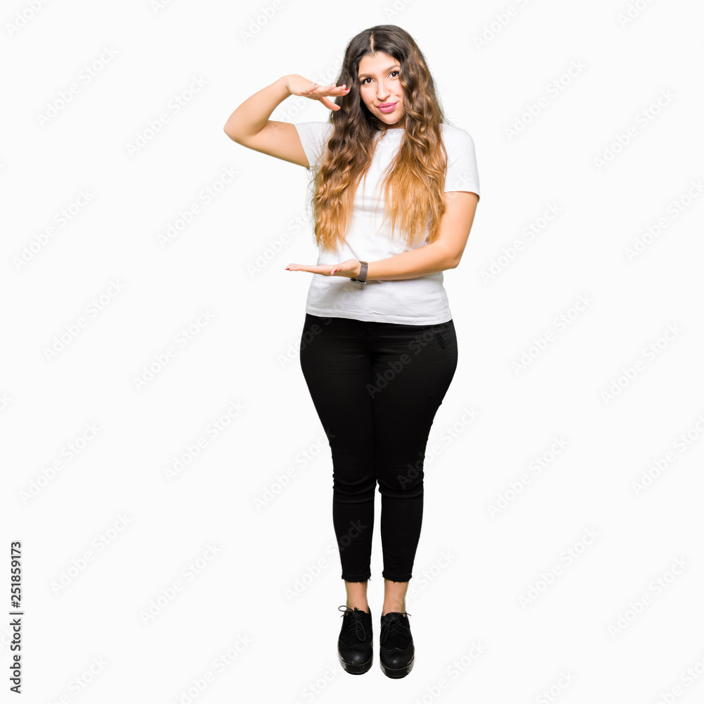Young beautiful woman wearing casual white t-shirt gesturing with hands showing big and large size sign, measure symbol. Smiling looking at the camera. Measuring concept. Young beautiful woman wearing casual white t-shirt gesturing with hands showing big and large size sign, measure symbol. Smiling looking at the camera. Measuring concept.