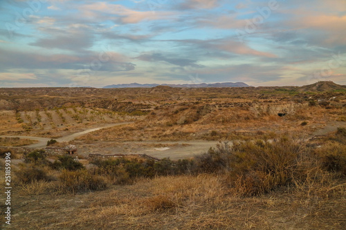 a path leads through a ruff steppe landscape with hills and blue light cloudy sky