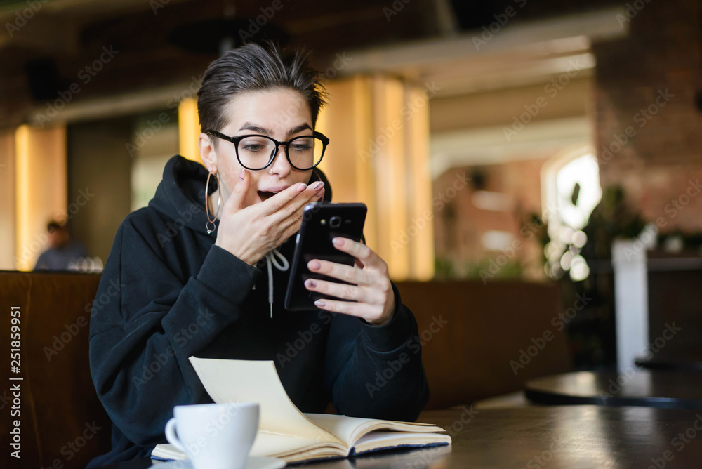Surprised shortcut hipster young girl getting shocked sms while reading book
