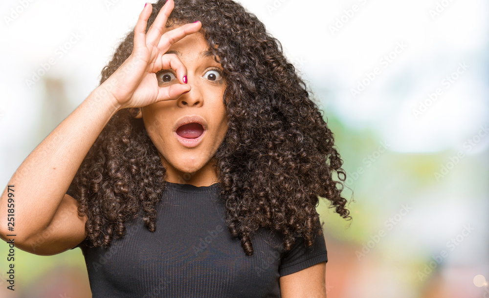 Young beautiful woman with curly hair doing ok gesture shocked with surprised face, eye looking through fingers. Unbelieving expression. Young beautiful woman with curly hair doing ok gesture shocked with surprised face, eye looking through fingers. Unbelieving expression.