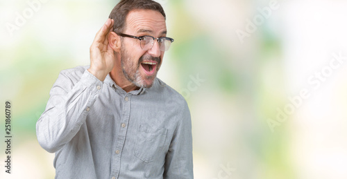 Handsome middle age elegant senior man wearing glasses over isolated background smiling with hand over ear listening an hearing to rumor or gossip. Deafness concept.