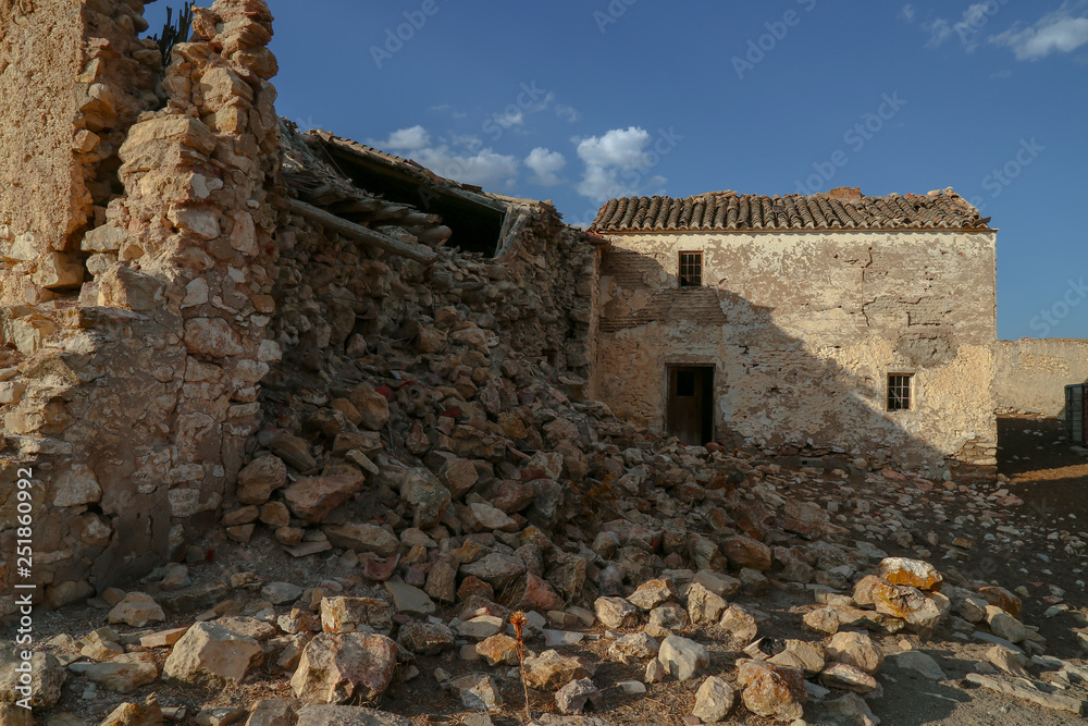 pile of stones with cracked wall and ruins of old farm house on a sunny day with blue sky and small clouds
