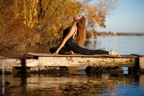 Young woman practicing yoga exercise at quiet pier in autumn park