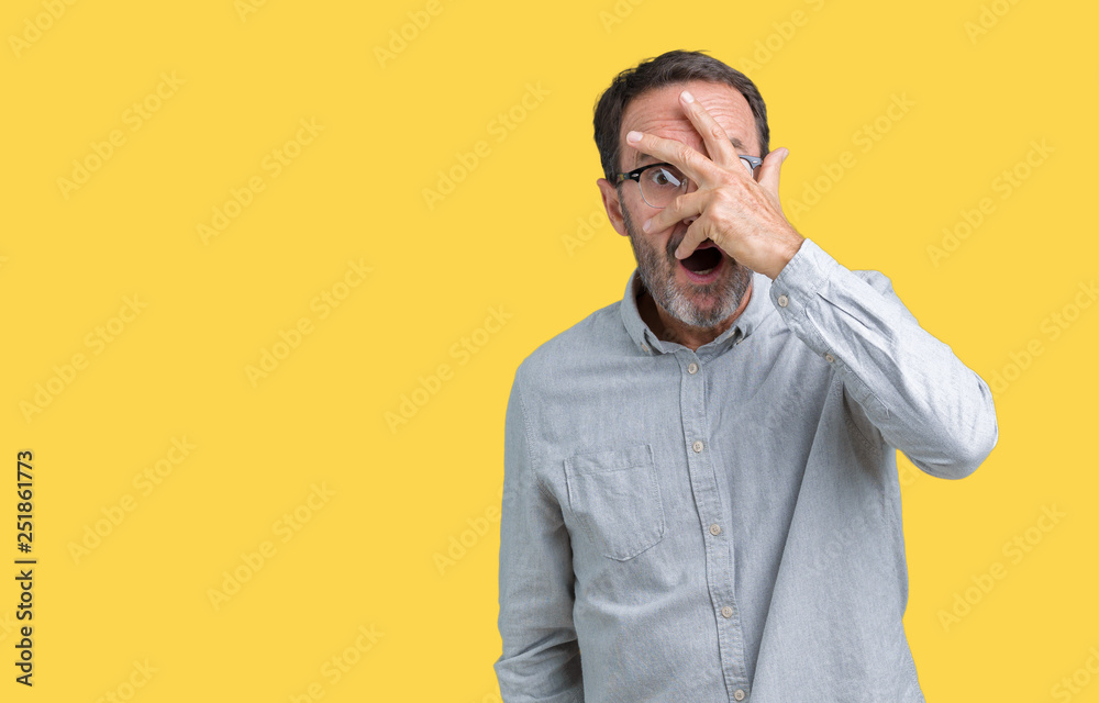 Handsome middle age elegant senior man wearing glasses over isolated background peeking in shock covering face and eyes with hand, looking through fingers with embarrassed expression. Handsome middle age elegant senior man wearing glasses over isolated background peeking in shock covering face and eyes with hand, looking through fingers with embarrassed expression.