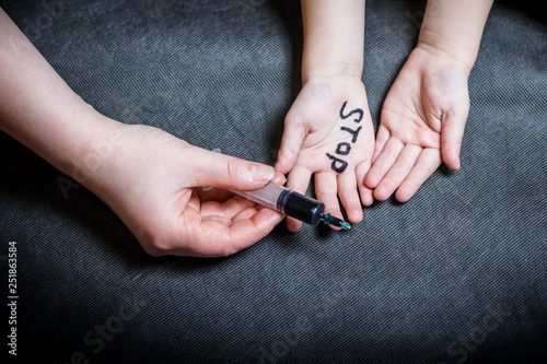 child's hand on the palm is written stop. the other holds a syringe with dark solutions.