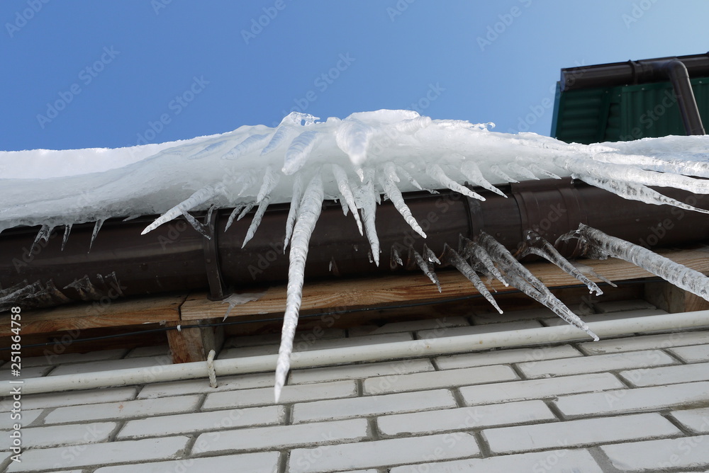 Transparent icicles on a roof on a blue sky background