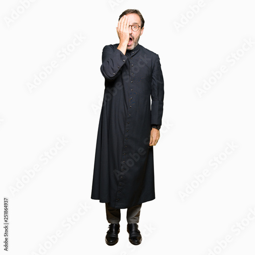 Middle age priest man wearing catholic robe Yawning tired covering half face, eye and mouth with hand. Face hurts in pain.