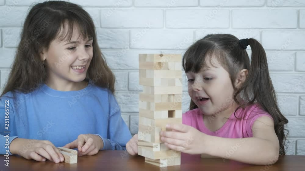 Children play with wooden blocks. Cute little sisters are playing an educational board game balance. Children play with wooden blocks. Cute little sisters are playing an educational board game balance.