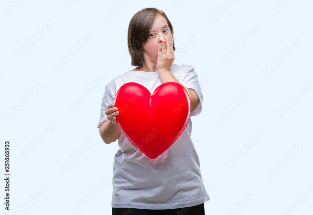 Young adult woman with down syndrome holding red heart over isolated background cover mouth with hand shocked with shame for mistake, expression of fear, scared in silence, secret concept Young adult woman with down syndrome holding red heart over isolated background cover mouth with hand shocked with shame for mistake, expression of fear, scared in silence, secret concept