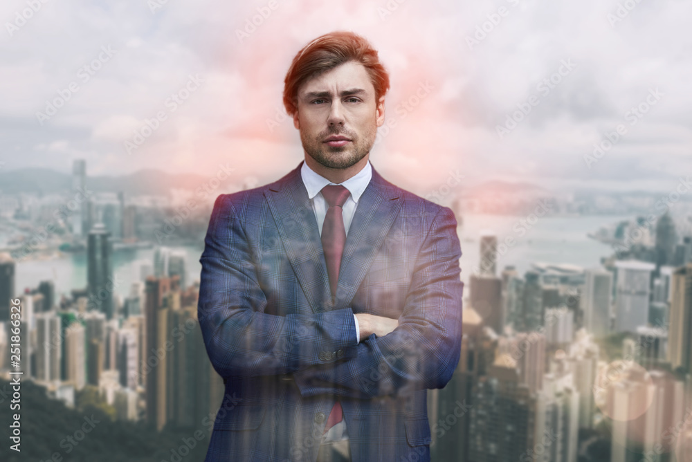Confident and succesful. Close-up portrait of attractive man in suit keeping his arms crossed while standing against of cityscape background. Confident and succesful. Close-up portrait of attractive man in suit keeping his arms crossed while standing against of cityscape background.