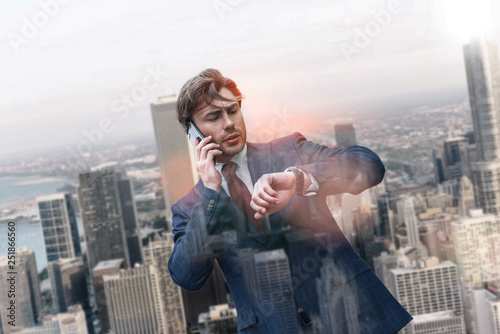 Lait again. Successful caucasian businessman in classic suit talking by phone and looking at his watch while standing against of cityscape background