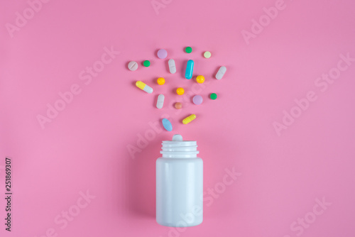 Colored pills, tablets and white bottle on pink background