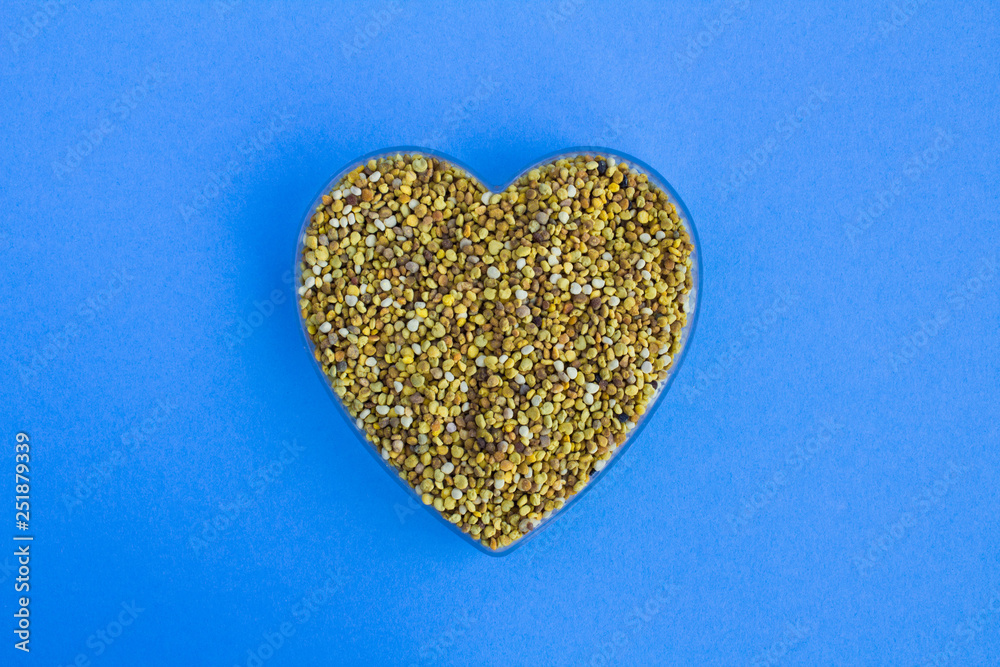 Bee pollen in the heart shape on the blue background.Top view.Copy space. Bee pollen in the heart shape on the blue background.Top view.Copy space.